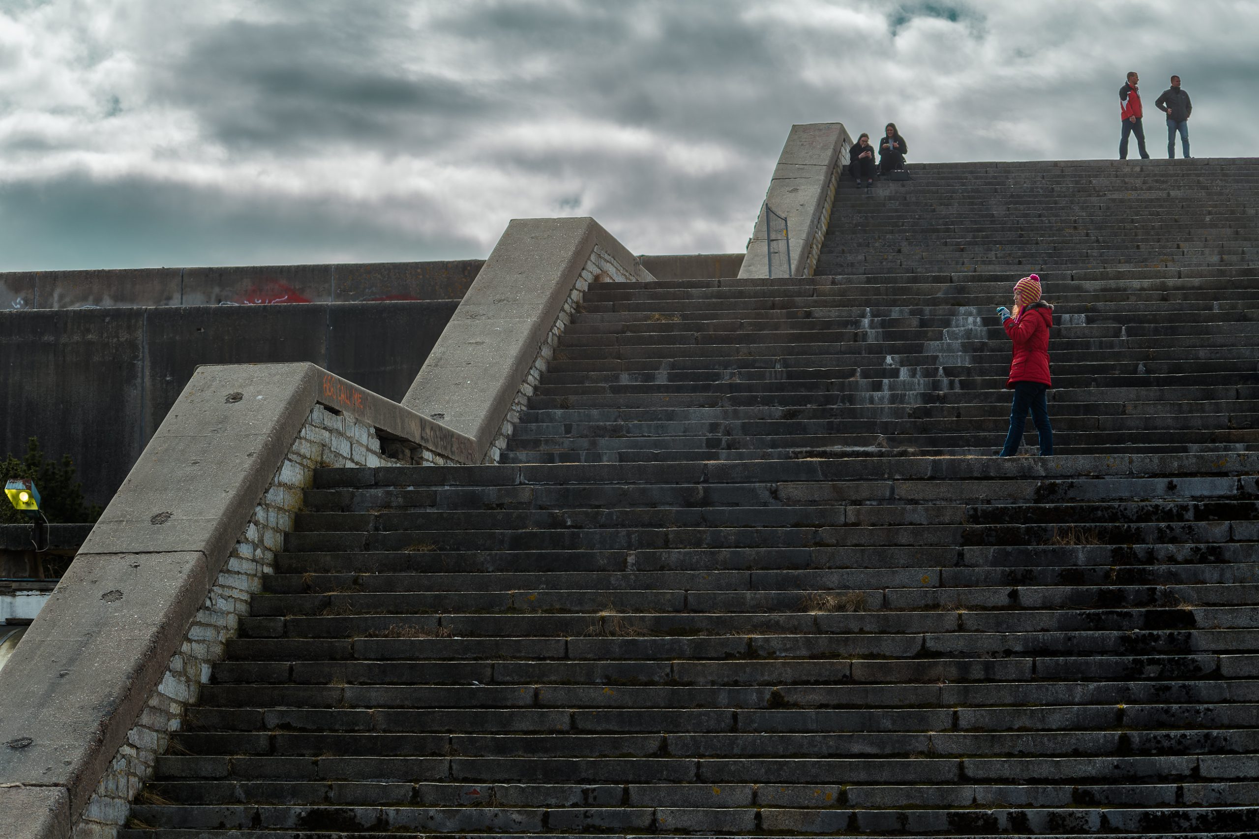 Approaching the Linnahall from the north. Three long tiers of stairs lead to the roof. On one of them a young girl in a red coat and wool hat pauses to look around