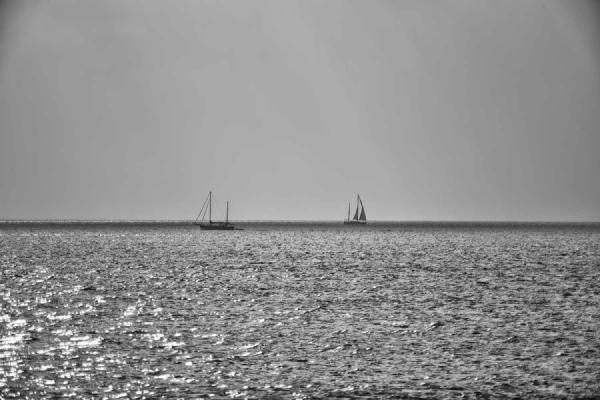 Two boats move slowly through a quiet sea illuminated by sun rays