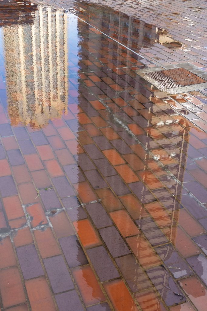 Two of the Barbican Estate towers' reflections are shown in a puddle