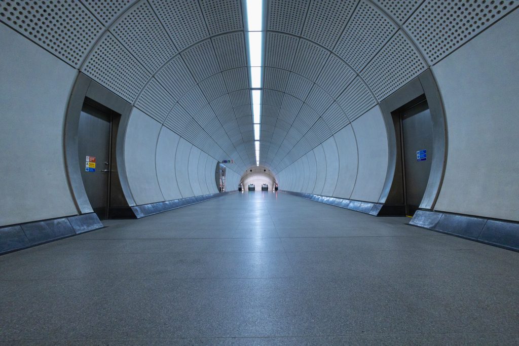 A below standing waist height photograph of a tunnel leading to the top of two escalators in the distance